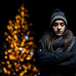 Woman in front of lit up tree, looks sad and lonely